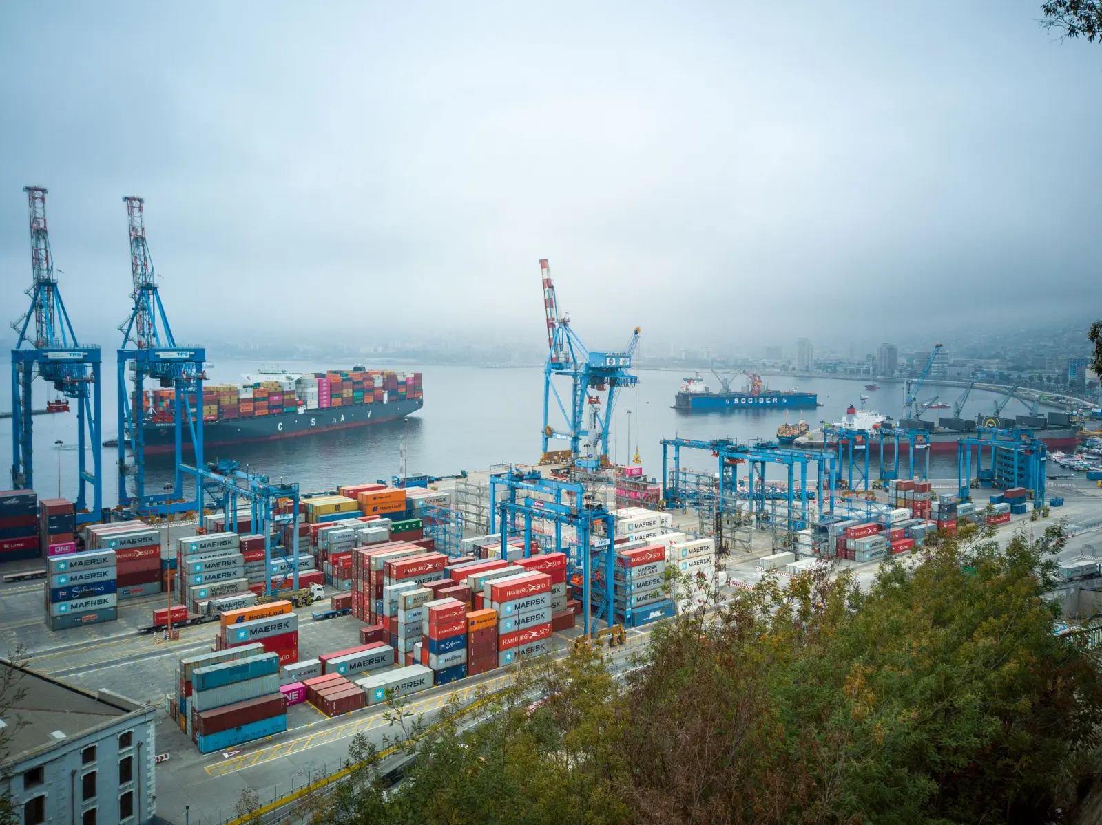 A cargo port with container stacks and quay cranes.