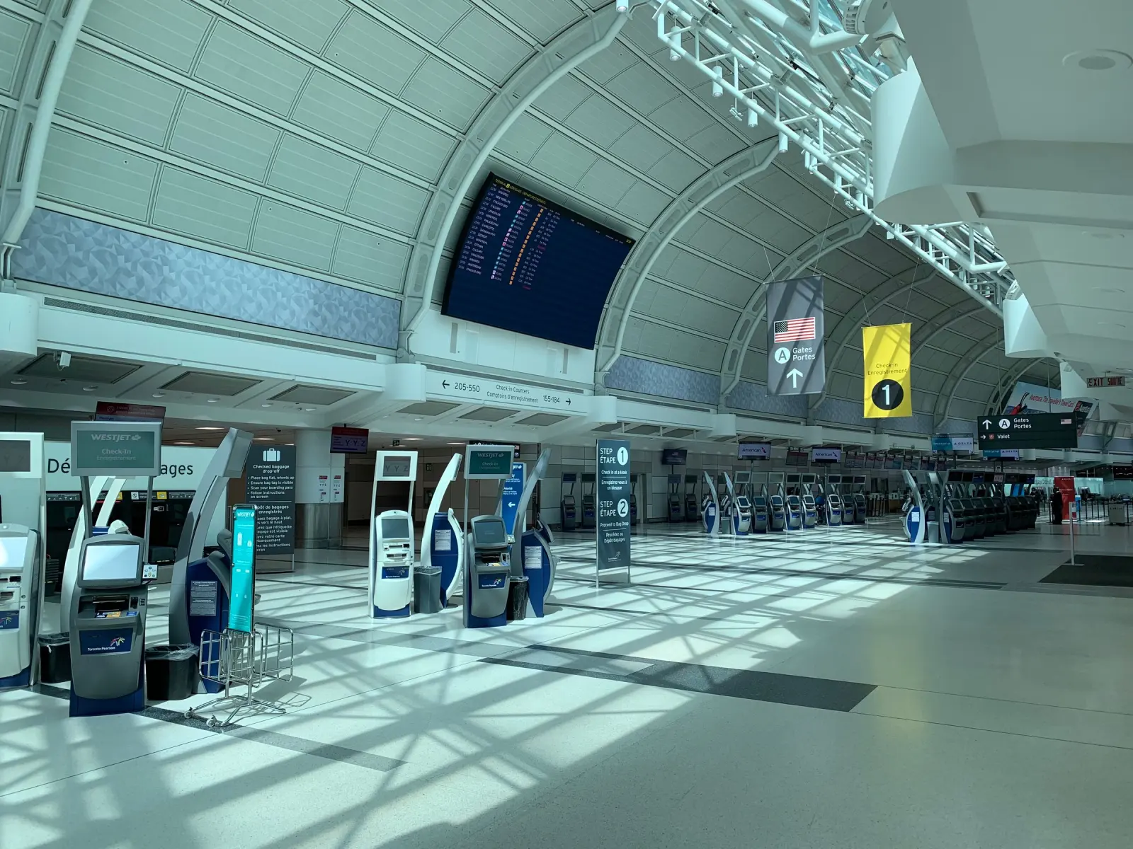 A bright airport terminal hall with check-in kiosks.