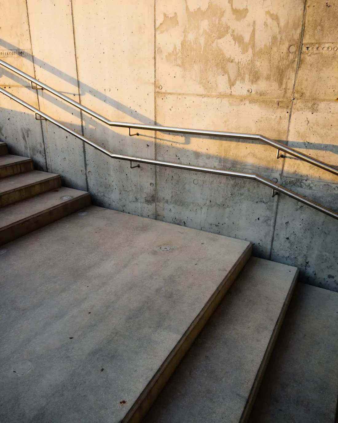 A concrete staircase with a metal handrail and geometric shadows.