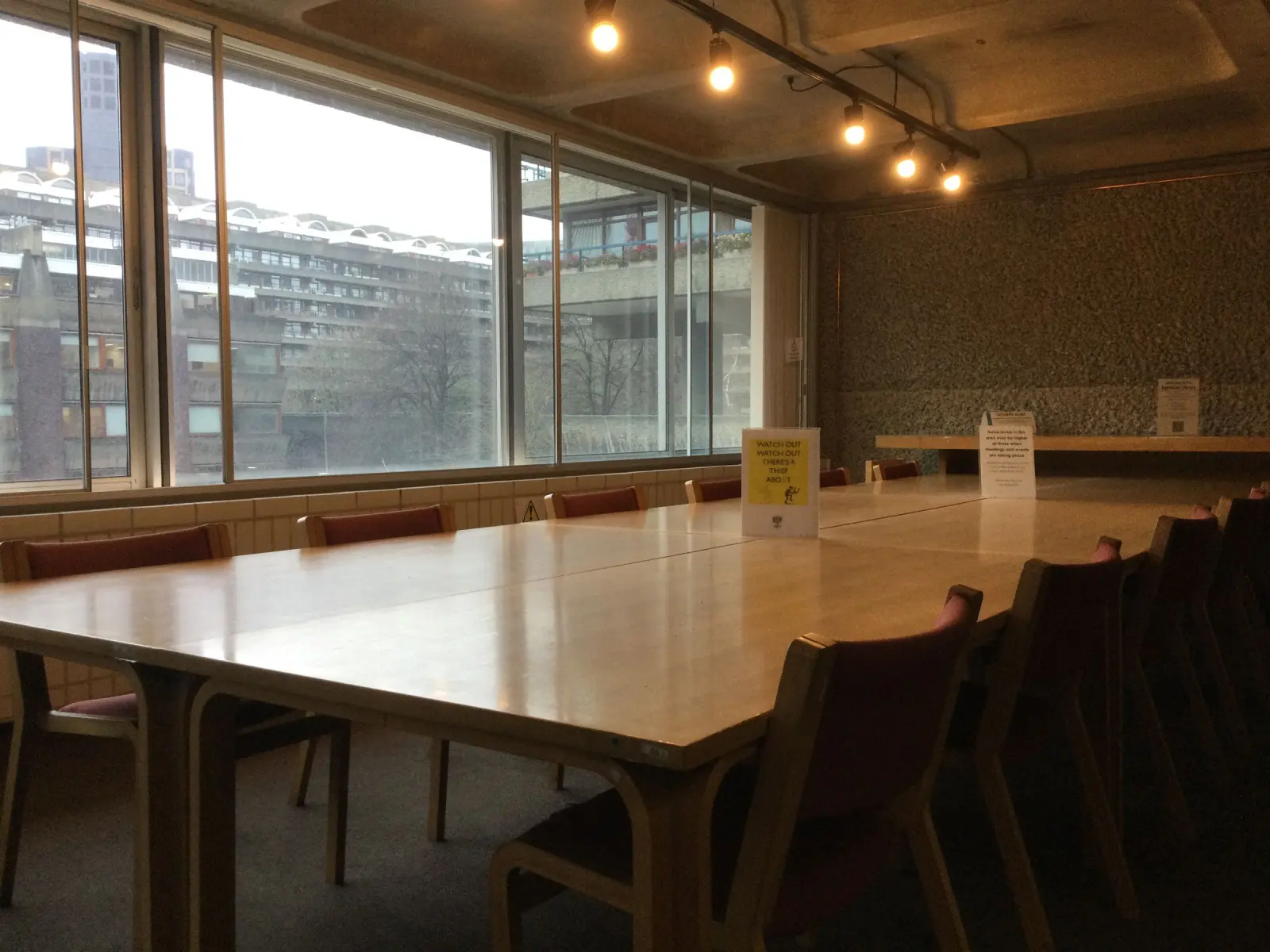 An empty conference room with a long table and tall windows.